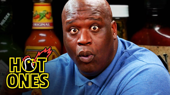 Shaq tries not to make a face while eating Hot Wings on the Hot Ones!