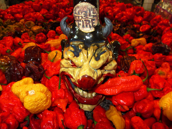 Hellfire Hot Sauce artisan sculpted demon bottle surrounded by chili peppers